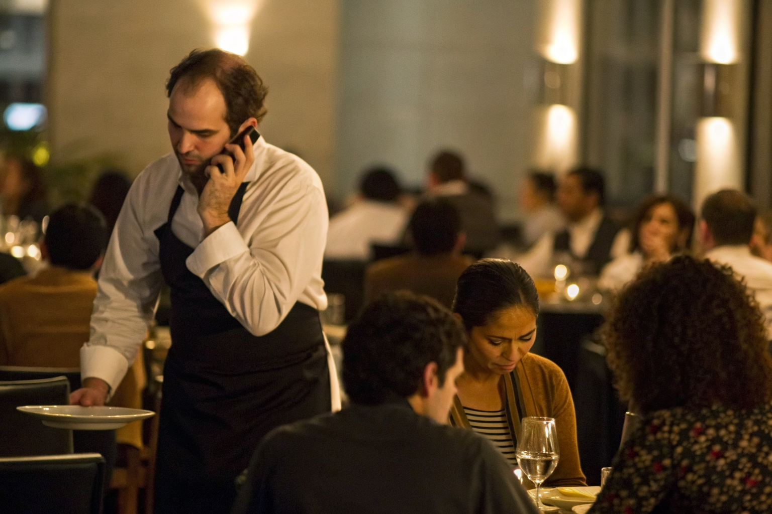 Busy restaurant host seating guests, phone ringing.